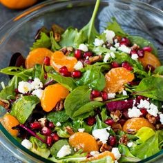 a salad with oranges, spinach and feta cheese in a glass bowl