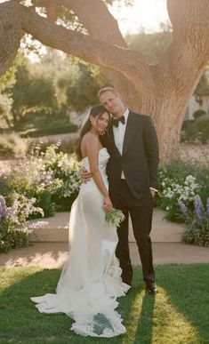 a bride and groom pose for a photo in front of a tree at their wedding