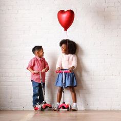 two children standing next to each other with a heart shaped balloon attached to the handlebars