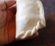 a hand holding a piece of food on top of a wooden table