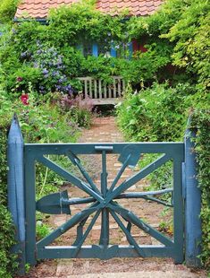 an iron gate in front of a house with flowers growing on the sides and bushes surrounding it