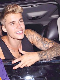 a person sitting in a car with tattoos on his arm and chest, smiling at the camera