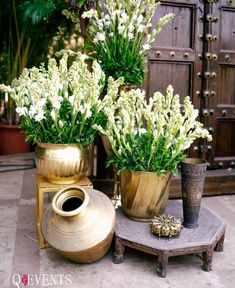 two vases with flowers are sitting on a small table next to another potted plant