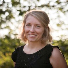 a woman with blonde hair smiling at the camera in front of some trees and grass