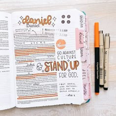 an open bible with writing on it next to two pens and markers, sitting on top of a wooden table