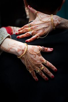 a woman with her hands covered in henna and rings on her chest, holding onto another person's arm