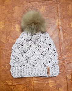 a white crocheted hat with a green pom - pom on top