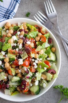 a white bowl filled with salad next to silverware and fork on top of a table