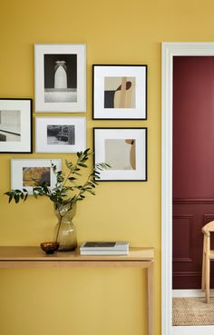 an entryway with yellow walls and pictures on the wall, plants in vase next to door