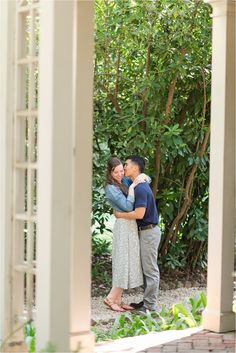 a man and woman embracing each other in front of some trees with greenery behind them