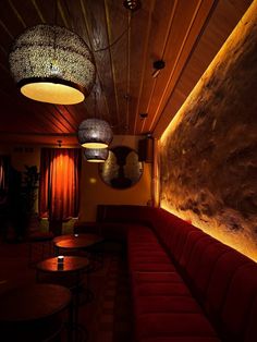 a dimly lit room with red couches and round lamps hanging from the ceiling above