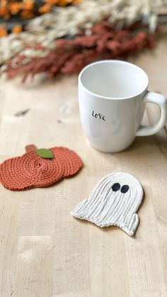 there is a coffee cup with a knitted ghost next to it on the table