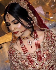 a woman in a red and gold bridal outfit with jewelry on her face, looking at the camera