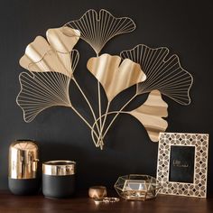 a table topped with gold vases next to a metal wall art piece on top of a black wall