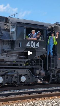 two men standing on the side of a train with their hands in the air and waving