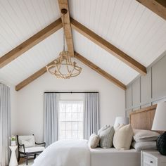 a bedroom with white walls and wood beams, a bed in the center is surrounded by pillows