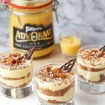 three small desserts are sitting on a table next to a jar of jelly and two glasses