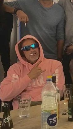 a man in a pink hoodie sitting at a table with bottles and glasses on it