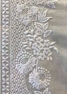 an embroidered piece of cloth with flowers and leaves on the side, in white thread