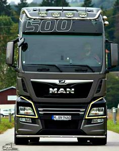 the front end of a large truck on a country road with houses in the background