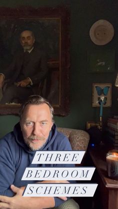 a man sitting on top of a couch next to a table in front of a painting