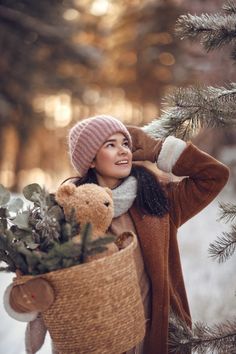 a woman holding a teddy bear in a basket next to a tree with snow on it