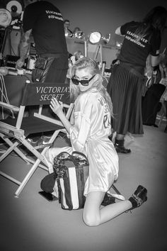 a woman sitting on the ground next to a chair holding a bag and wearing sunglasses