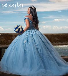 a woman in a blue dress is standing on a ledge looking at the ocean and sky