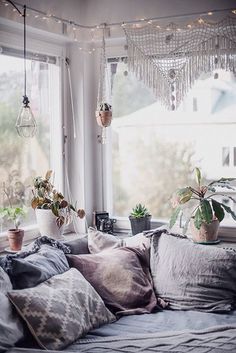 a couch with many pillows and plants in the window sill, next to a potted plant