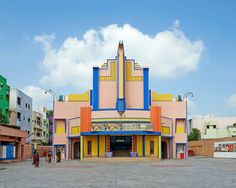 an old movie theater in the middle of a parking lot with people walking around it