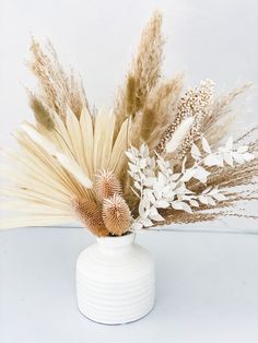 a white vase filled with dried flowers on top of a table