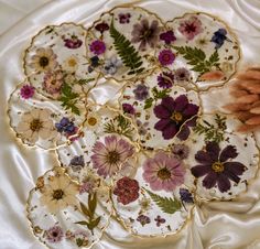 four decorative plates with flowers on them sitting on a white satin covered tablecloth,