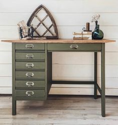 a green desk with drawers and a vase on it next to a white shipboard wall