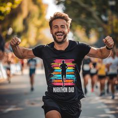 Introducing the Marathon T-Shirt, a perfect blend of comfort, style, and motivation for all the dedicated dads who conquer the roads. Available with express delivery in navy, black and dark grey heather, this dad runner t-shirt features a bold and inspiring design, a silhouetted runner against a striped colored background with a shirt that proudly displays "Marathon Dad", a graphic that symbolizes the relentless spirit of marathon running dads. The vibrant colors and sharp details of the print m Marathon Tshirt Design, Marathon T Shirt Design, Short Sleeve Letter Print T-shirt For Marathon, Graphic Tee Crew Neck T-shirt For Running, Marathon T-shirt, Marathon Runners, Running Gifts, Marathon Running, Marathon Training