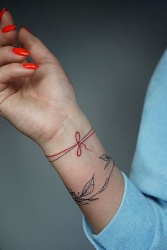 a woman's wrist with a red ribbon on it and an arrow tattooed on the wrist