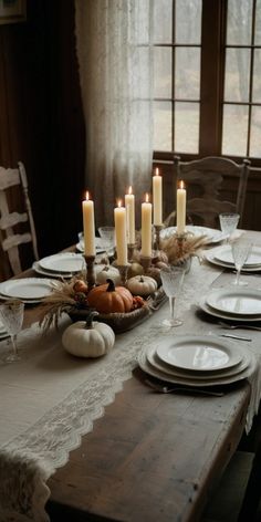 a table set with plates, candles and pumpkins