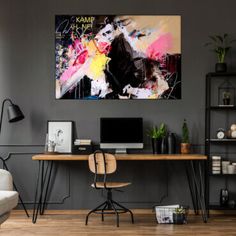 a desk with a computer on top of it in front of a wall mounted painting