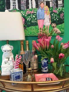 a table with flowers, candles and bottles on it in front of a green wall