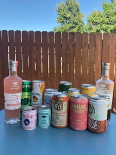 a table topped with lots of different types of drinks next to a wooden privacy fence