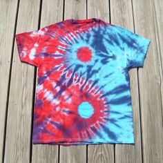 a red, blue and white tie - dyed shirt sitting on top of a wooden deck