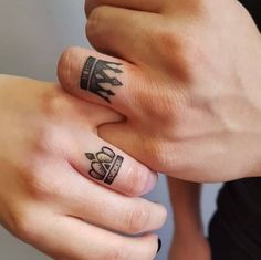 two people with tattoos on their fingers holding each other's hands and one has a crown tattoo on it