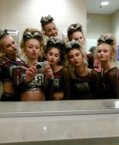 a group of cheerleaders taking a selfie in front of a bathroom mirror