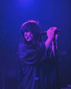 a woman with long hair holding a microphone in her right hand while standing on stage