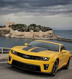 a yellow chevrolet camaro is parked on the side of the road near an island