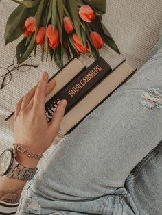 a person sitting on a couch with a book in their lap and flowers behind them