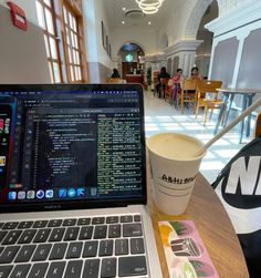 an open laptop computer sitting on top of a wooden table next to a cup of coffee