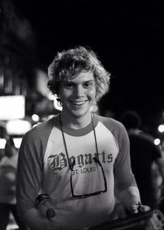 a young man holding a skateboard in his right hand and smiling at the camera