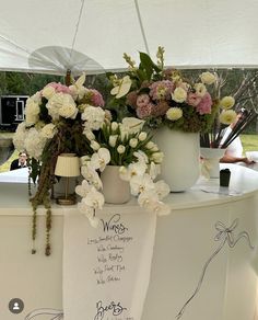 flowers are sitting on top of a table under a white tent at an outdoor event