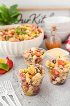 four plastic cups filled with pasta salad on top of a table next to silverware