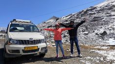 two people standing in front of a white van on the side of a mountain road